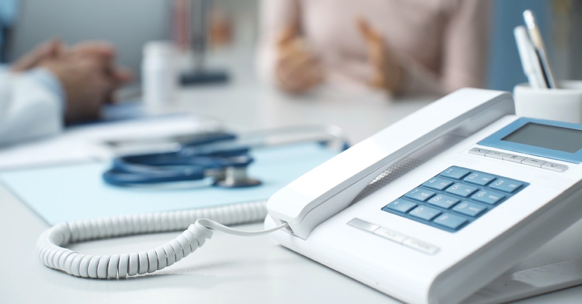 medical office telephone on a desk with office supplies, and people talking in the background