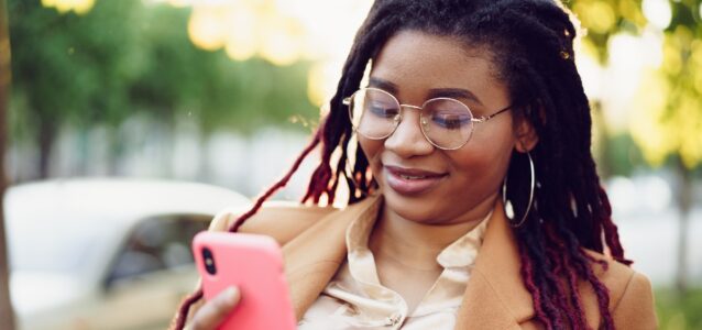 Person standing outdoors with a phone looking at the screen.