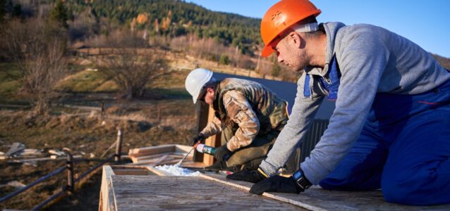Roofing crew on a roof installing thermal insulation to protect from the elements.